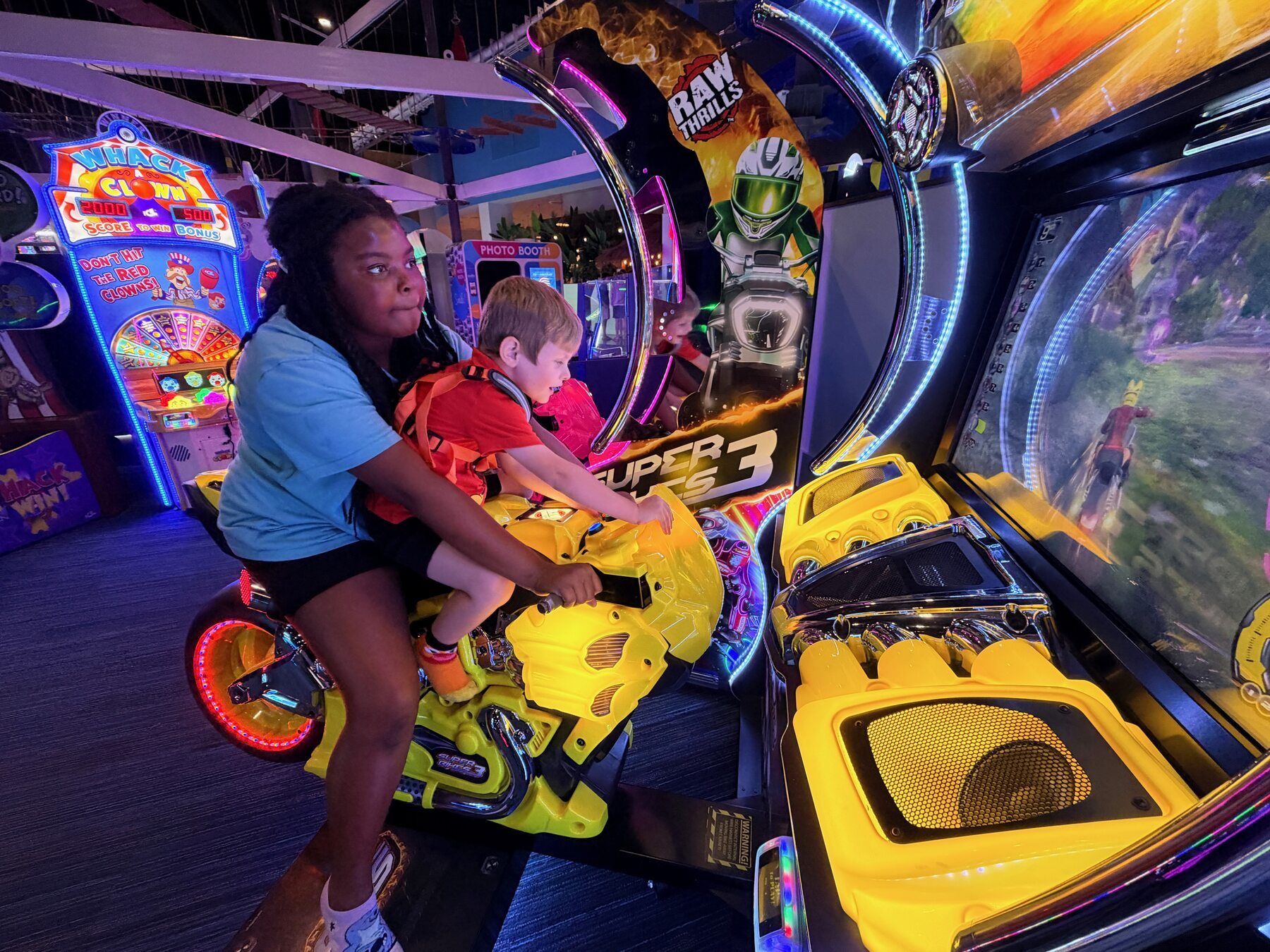 An adult helps a young child play a motorcycle arcade game at High Tides & Good Vibes in Surf City
