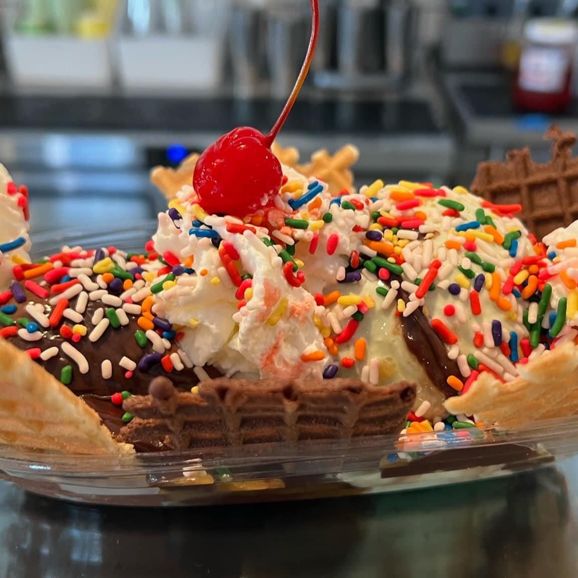 An ice cream sundae with sprinkles, whipped cream and a cherry in a waffle bowl