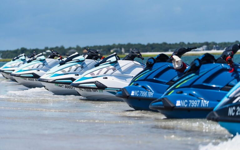 A row of jet skis beached in shallow sound water