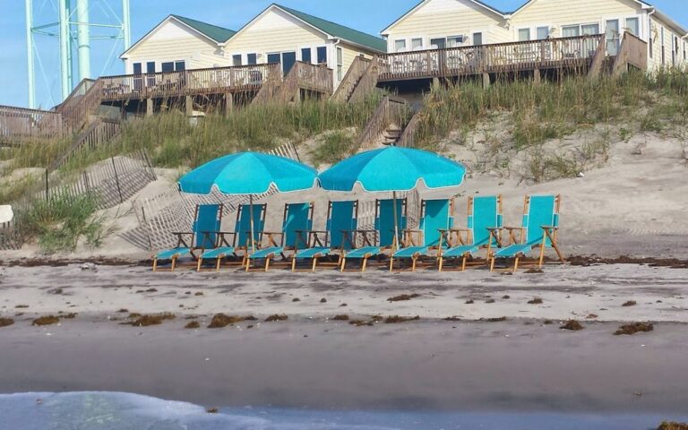 Rows of teal beach chairs and umbrellas set up below the dunes