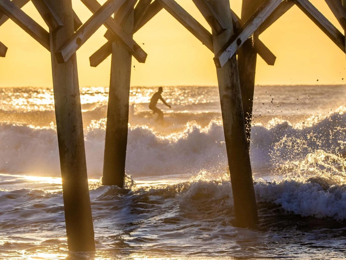 Waves breaking through pier pilings at golden hour