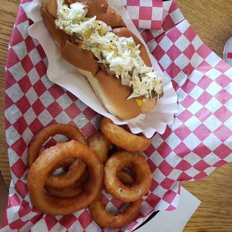 A hot dog with chili and slaw and a side of onion rings in a checkered basket